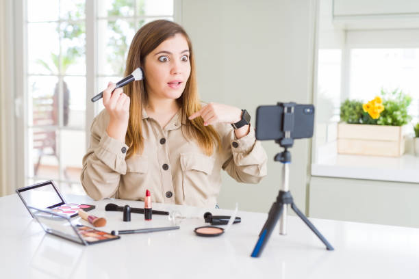 istock Beautiful young influencer woman recording make up video tutorial with surprise face pointing finger to himself 1143481278