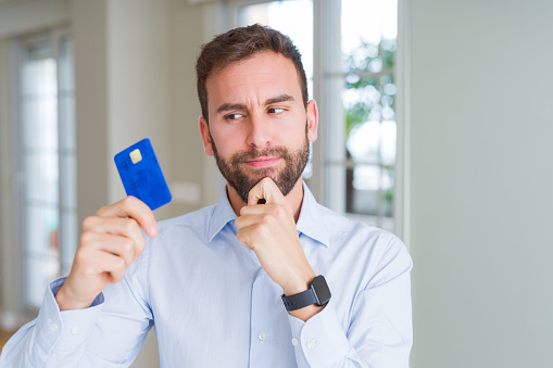 Handsome business man holding credit card serious face thinking about question, very confused idea