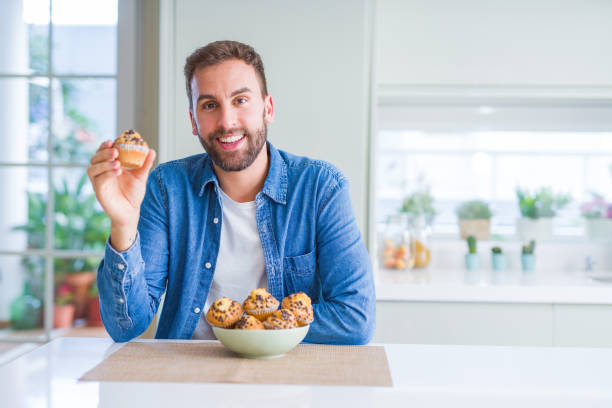 istock Handsome man eating chocolate chips muffin with a happy face standing and smiling with a confident smile showing teeth 1143482739