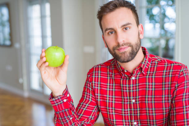 istock Handsome man eating fresh healthy green apple with a confident expression on smart face thinking serious 1143482946