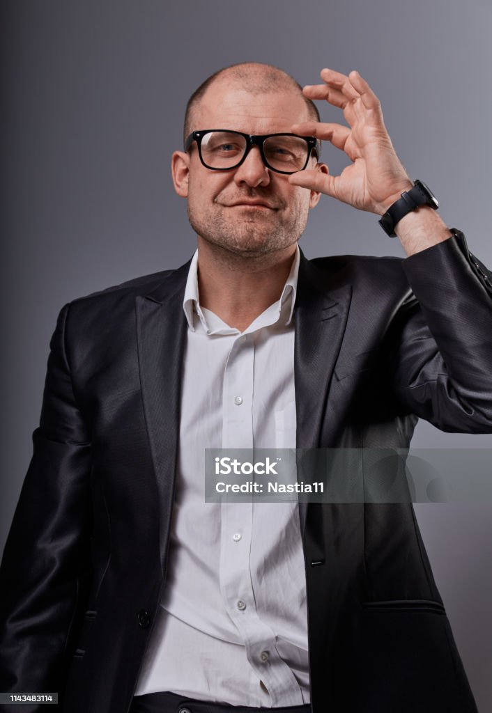 Thinking bald business man looking serious in eyeglasses in suit on grey background. Closeup Thinking smiling bald business man looking serious in eyeglasses in suit on grey background. Closeup portrait Hooligan Stock Photo