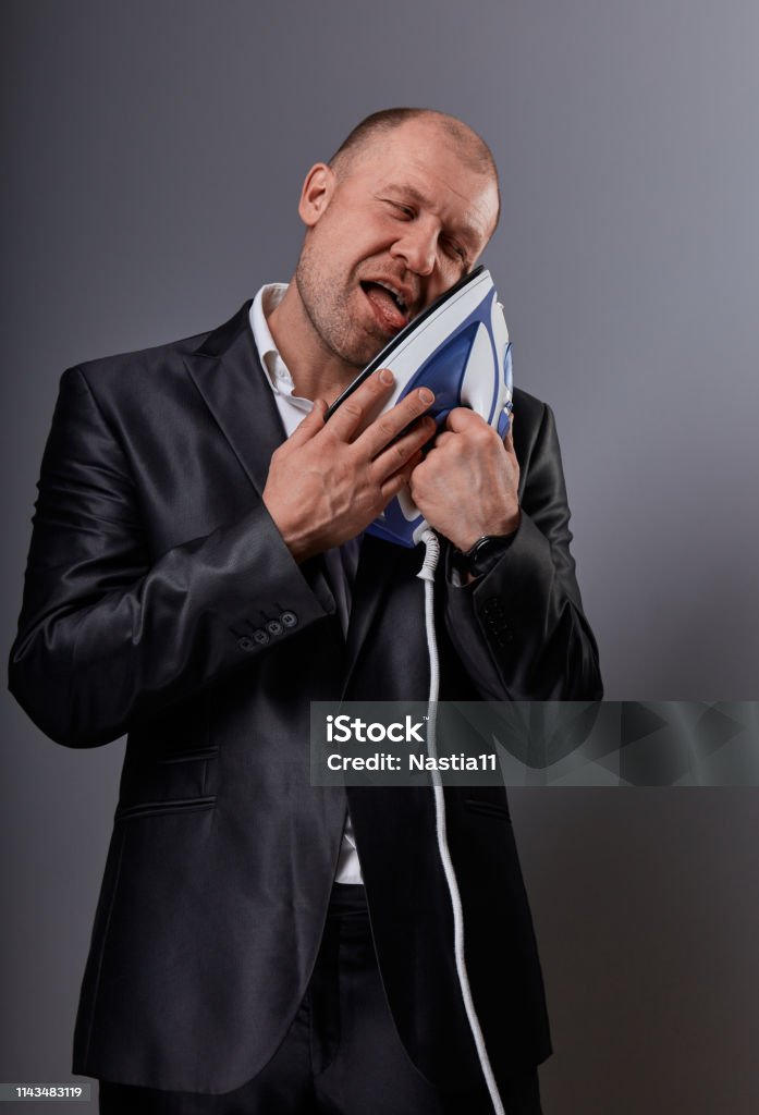 Bald crazy comic business man holding the home comfort iron and caressing it with love and closed enjoying eyes in suit on grey background. Closeup. Perfec husband Bald crazy comic business man holding the home comfort iron and caressing it with love and closed enjoying eyes in suit on grey background. Closeup. Perfec husband loving the home domestic work Adult Stock Photo