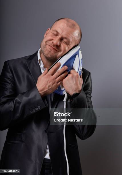 Bald Happy Comic Business Man Holding The Home Comfort Iron And Caressing It With Love And Closed Enjoying Eyes In Suit On Grey Background Closeup Perfec Husband Stock Photo - Download Image Now