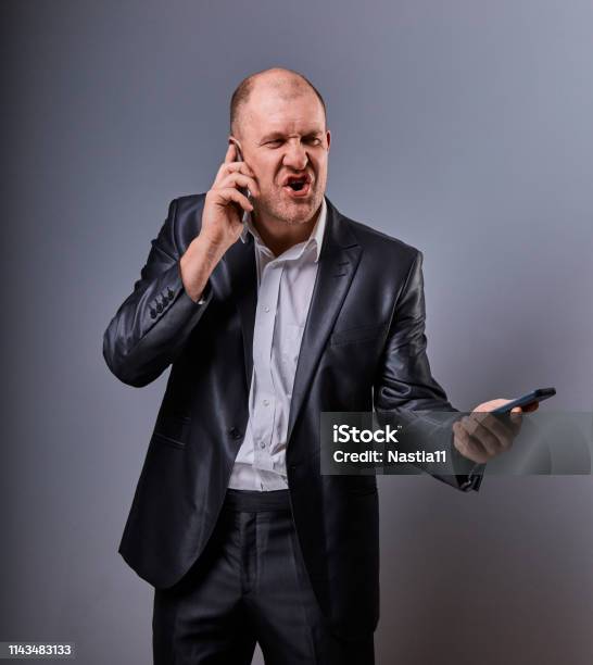 Unhappy Loud Crying Angry Business Man Talking On Mobile Phone Very Emotional In Office Suit On Grey Background Closeup Stock Photo - Download Image Now