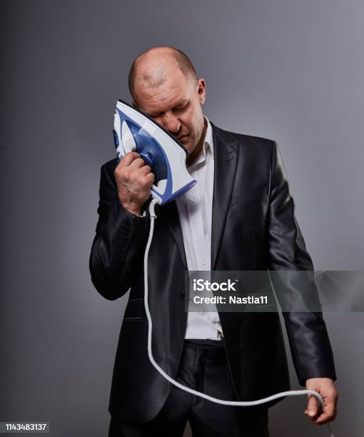 Bald Fun Tired Unhappy Loser Failed Business Man Punishing Himself Holding The Home Iron Near The Face In Suit On Grey Background Closeup Stock Photo - Download Image Now