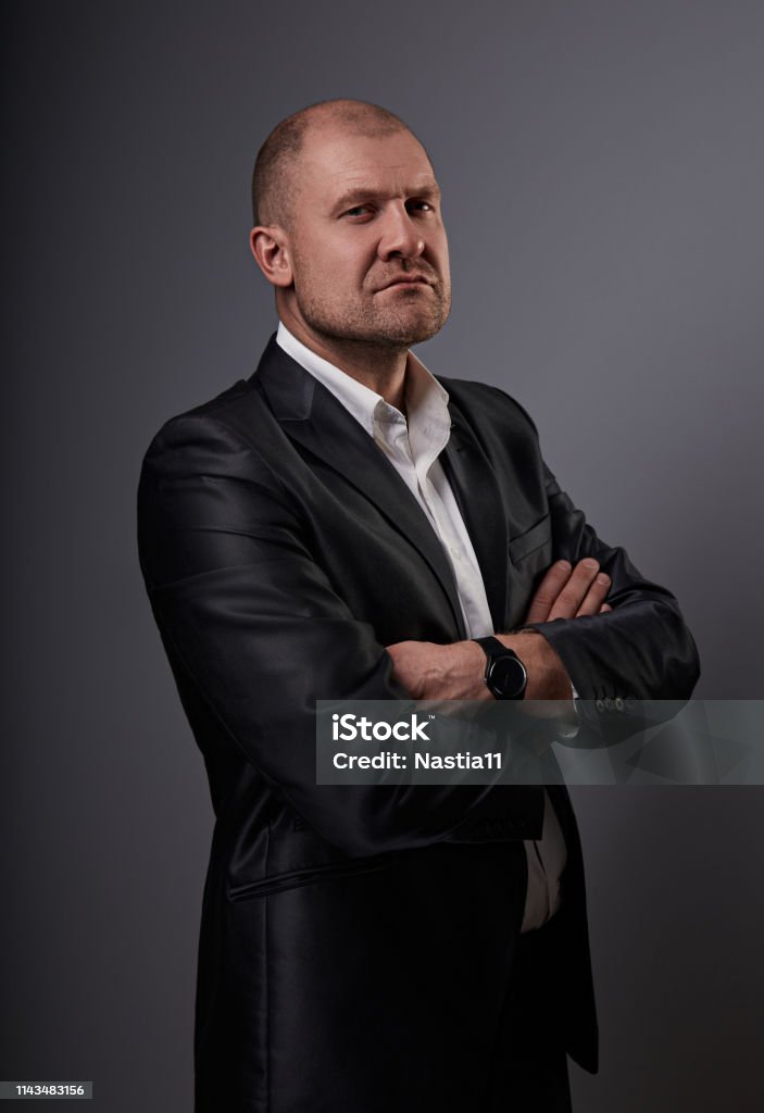 Serious bald business man with folded arms in suit on grey background. Closeup Serious bald thinking business man with folded arms in suit on grey background. Closeup portrait Adult Stock Photo