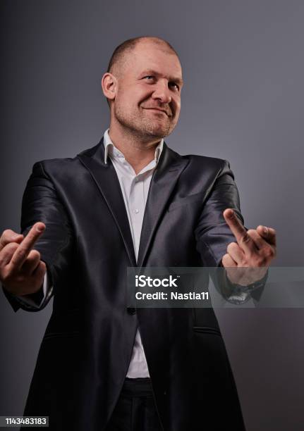 Fun Comic Bald Business Man In Black Suit Showing The Finger Fuck Sign On Grey Background Closeup Stock Photo - Download Image Now