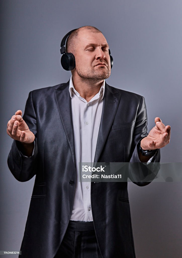 Business man listening the music in wireless earphone and trying relax he showing the hands yoga sign zen on grey studio background. Closeup Business man listening the music in wireless earphone and trying relax he showing the hands yoga sign zen on grey studio background. Closeup portrait Actor Stock Photo