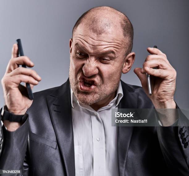 Turn Nasty Loud Crying Angry Business Man Talking On Two Mobile Phone Very Emotional In Office Suit On Grey Background Closeup Stock Photo - Download Image Now