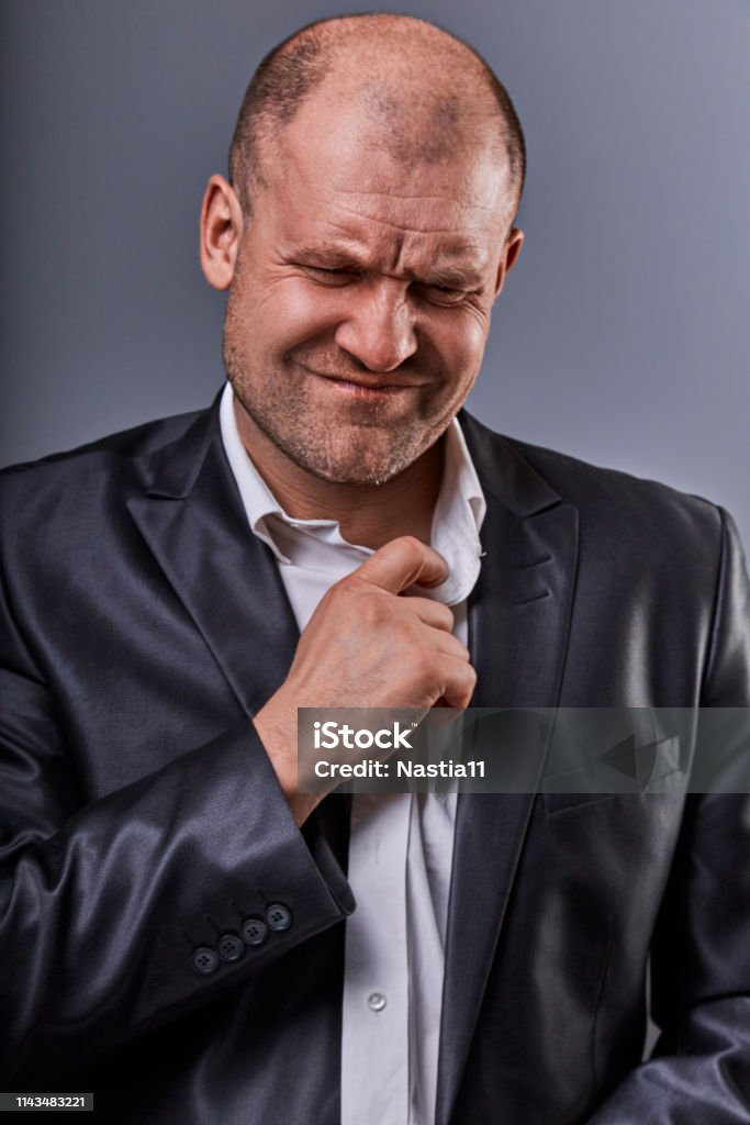 Unhappy stressed bald angry business man pulling the shirt collar with very bad emotions in office suit on grey studio background. Closeup Unhappy stressed bald angry business man pulling the shirt collar with very bad emotions in office suit on grey studio background. Closeup portrait Businessman Stock Photo