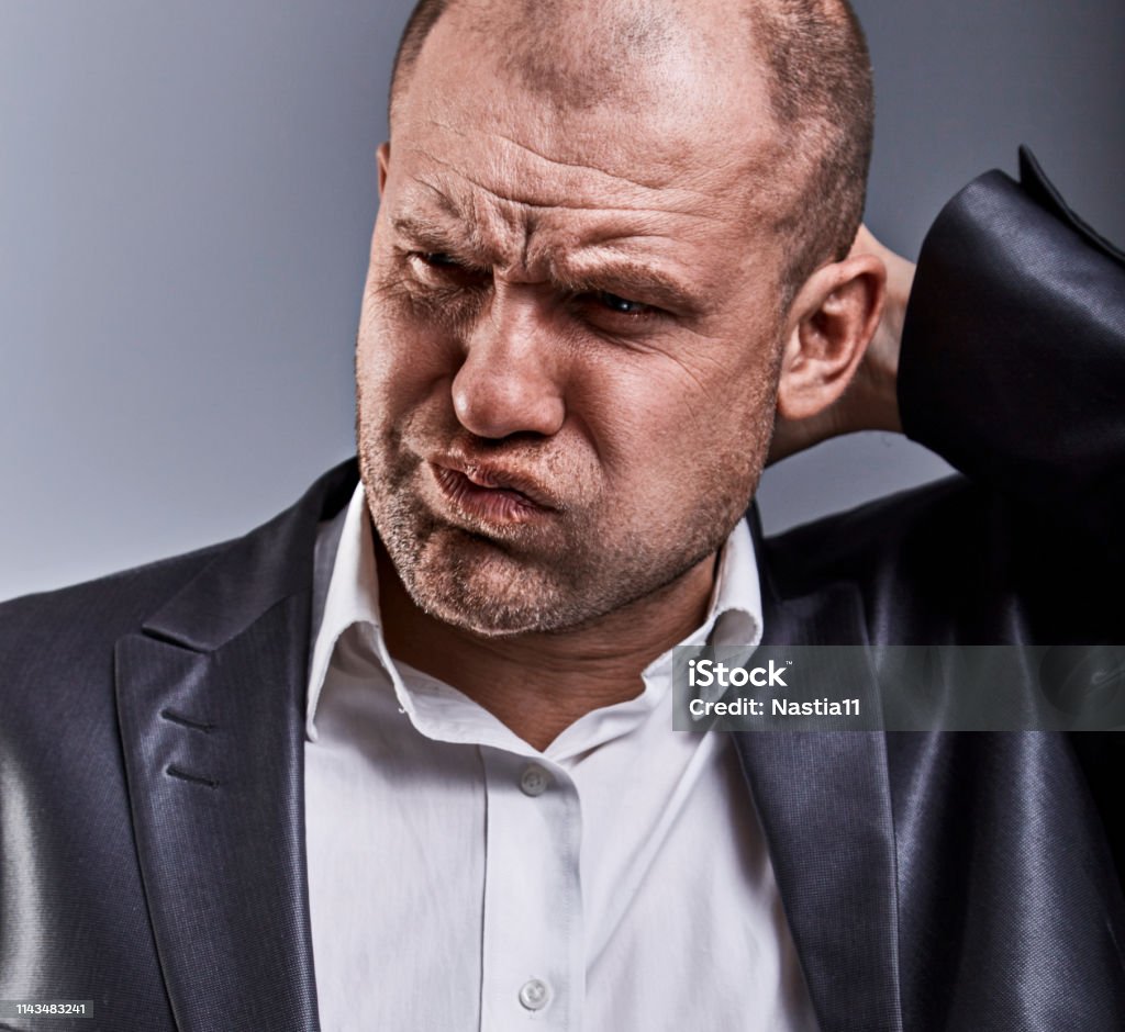 Unhappy stressed bald angry business man to scratching the head with very bad emotions in office suit on grey studio background. Closeup face portrait Unhappy stressed bald angry business man to scratching the head with very bad emotions in office suit on grey studio background. Closeup toned face portrait Businessman Stock Photo