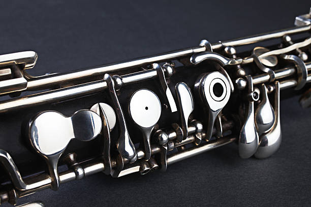 Close up of a person playing an oboe. Image shows the reed and the hand and finger positions. Studio shot on a black background.