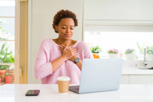 istock Young african american woman working using computer laptop smiling with hands on chest with closed eyes and grateful gesture on face. Health concept. 1143484936