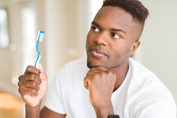 istock African american man holding toothbrush serious face thinking about question, very confused idea 1143488988