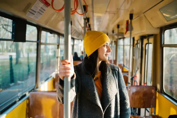 Photo of Young woman standing in a wagon of a driving tramway. Transportation, travel and lifestyle concept.