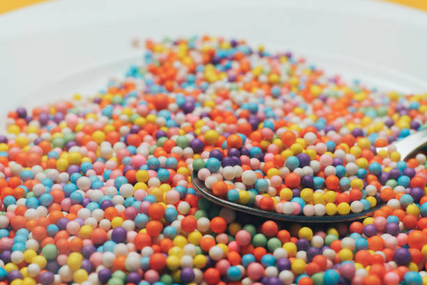 istock White plate and spoon with color preparations (vitamins, dyes, flavor enhancers, nutritional supplements, innovative technologies, candy sweets) on an orange background. Close up. 1143490688