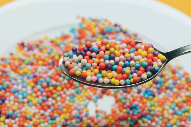 istock White plate and spoon with color preparations (vitamins, dyes, flavor enhancers, nutritional supplements, innovative technologies, candy sweets) on an orange background. Close up. 1143490758