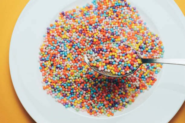 istock White plate and spoon with color preparations (vitamins, dyes, flavor enhancers, nutritional supplements, innovative technologies, candy sweets) on an orange background. 1143490779