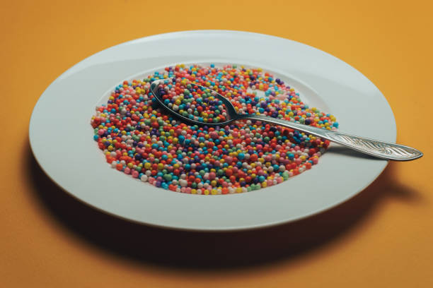 istock White plate and spoon with color preparations (vitamins, dyes, flavor enhancers, nutritional supplements, innovative technologies, candy sweets) on an orange background. 1143490907