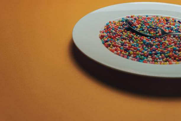 istock White plate and spoon with color preparations (vitamins, dyes, flavor enhancers, nutritional supplements, innovative technologies, candy sweets) on an orange background. 1143490968
