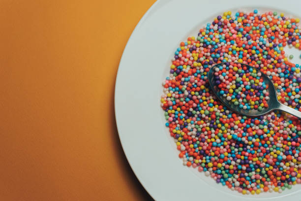 istock White plate and spoon with color preparations (vitamins, dyes, flavor enhancers, nutritional supplements, innovative technologies, candy sweets) on an orange background. 1143491217