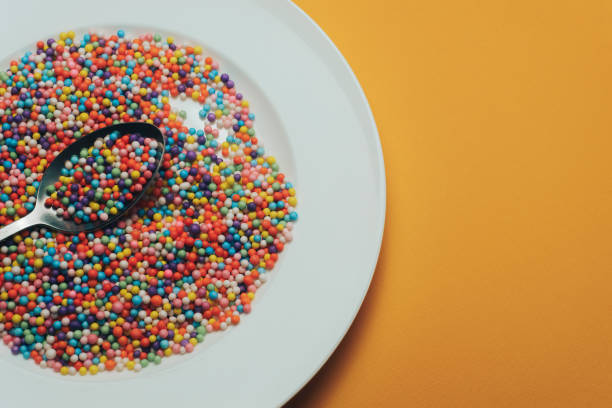 istock White plate and spoon with color preparations (vitamins, dyes, flavor enhancers, nutritional supplements, innovative technologies, candy sweets) on an orange background. 1143491655