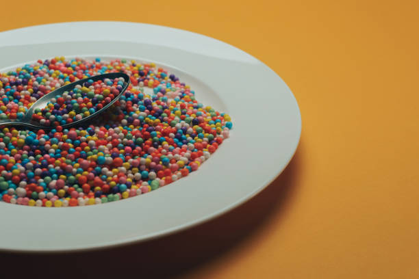 istock White plate and spoon with color preparations (vitamins, dyes, flavor enhancers, nutritional supplements, innovative technologies, candy sweets) on an orange background. 1143491737