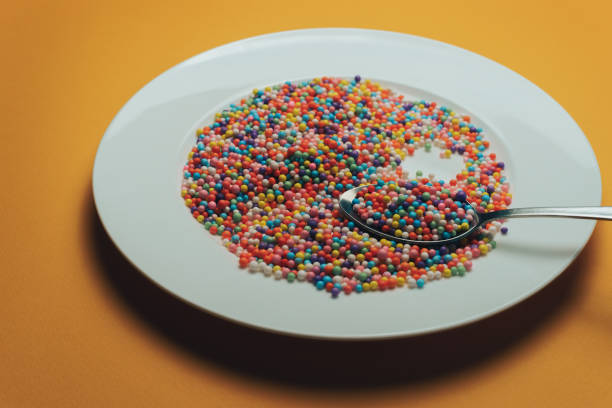 White plate and spoon with color preparations (vitamins, dyes, flavor enhancers, nutritional supplements, innovative technologies, candy sweets) on an orange background.