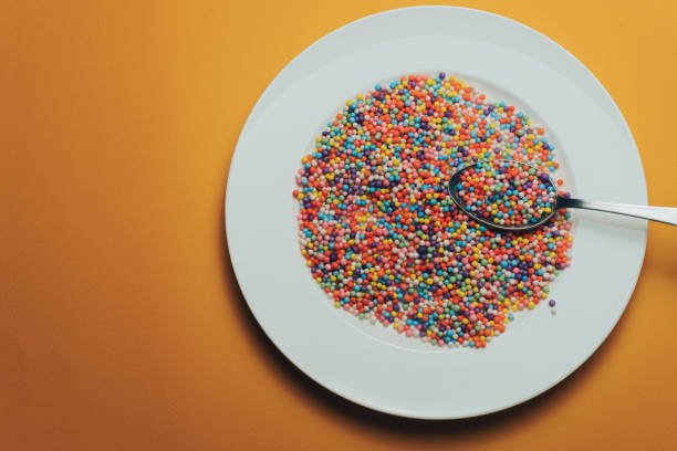 istock White plate and spoon with color preparations (vitamins, dyes, flavor enhancers, nutritional supplements, innovative technologies, candy sweets) on an orange background. 1143491878