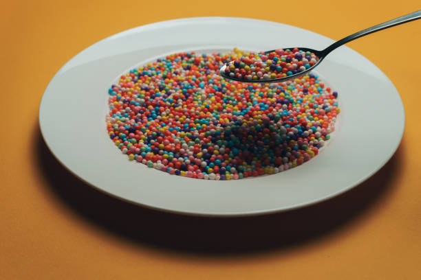 istock White plate and spoon with color preparations (vitamins, dyes, flavor enhancers, nutritional supplements, innovative technologies, candy sweets) on an orange background. 1143491907