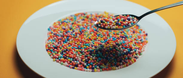 istock White plate and spoon with color preparations (vitamins, dyes, flavor enhancers, nutritional supplements, innovative technologies, candy sweets) on an orange background. 1143491963
