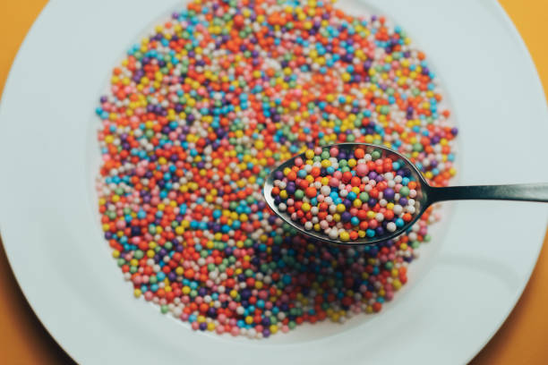 istock White plate and spoon with color preparations (vitamins, dyes, flavor enhancers, nutritional supplements, innovative technologies, candy sweets) on an orange background. 1143492033