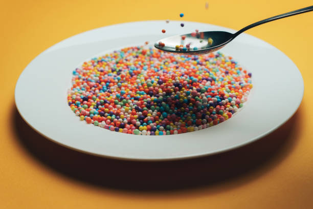 istock White plate and spoon with color preparations (vitamins, dyes, flavor enhancers, nutritional supplements, innovative technologies, candy sweets) on an orange background. 1143492171
