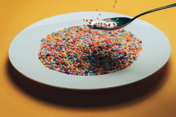 istock White plate and spoon with color preparations (vitamins, dyes, flavor enhancers, nutritional supplements, innovative technologies, candy sweets) on an orange background. 1143492195