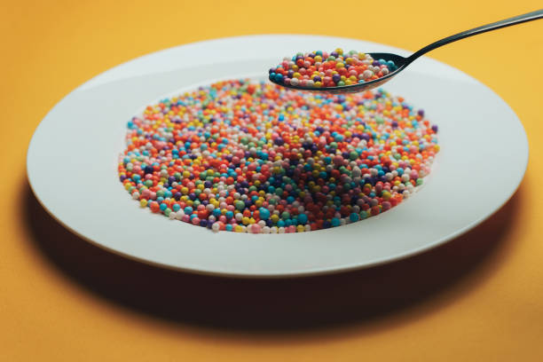 istock White plate and spoon with color preparations (vitamins, dyes, flavor enhancers, nutritional supplements, innovative technologies, candy sweets) on an orange background. 1143492241