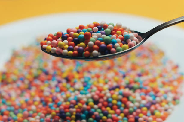 White plate and spoon with color preparations (vitamins, dyes, flavor enhancers, nutritional supplements, innovative technologies, candy sweets) on an orange background. Close up.