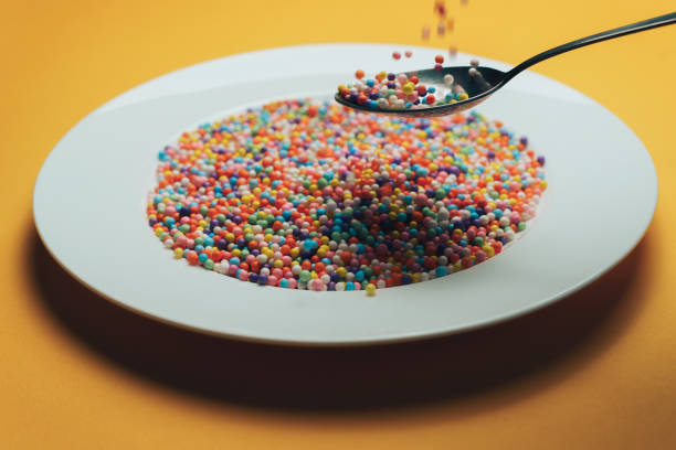 istock White plate and spoon with color preparations (vitamins, dyes, flavor enhancers, nutritional supplements, innovative technologies, candy sweets) on an orange background. 1143492559