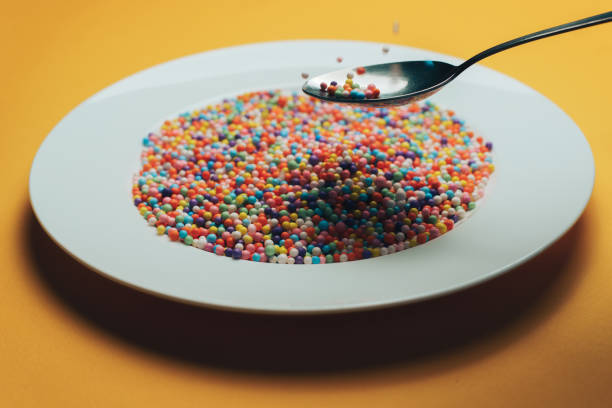 istock White plate and spoon with color preparations (vitamins, dyes, flavor enhancers, nutritional supplements, innovative technologies, candy sweets) on an orange background. 1143492648