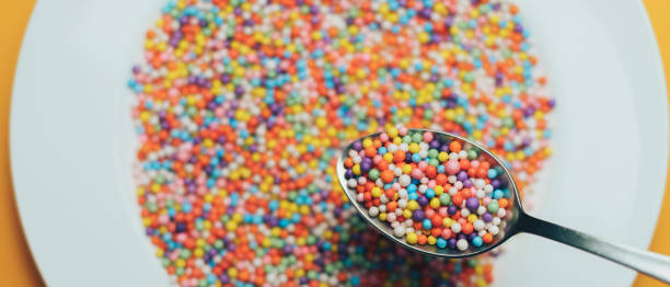 istock White plate and spoon with color preparations (vitamins, dyes, flavor enhancers, nutritional supplements, innovative technologies, candy sweets) on an orange background. 1143492697