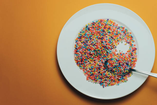 istock White plate and spoon with color preparations (vitamins, dyes, flavor enhancers, nutritional supplements, innovative technologies, candy sweets) on an orange background. 1143492913