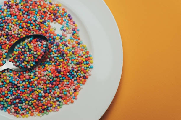 istock White plate and spoon with color preparations (vitamins, dyes, flavor enhancers, nutritional supplements, innovative technologies, candy sweets) on an orange background. 1143494063