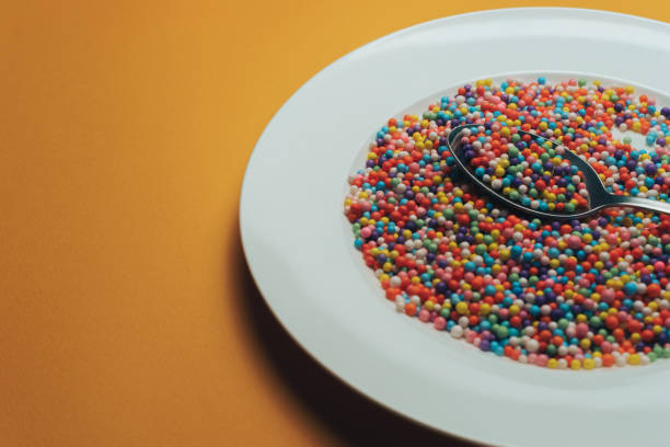 istock White plate and spoon with color preparations (vitamins, dyes, flavor enhancers, nutritional supplements, innovative technologies, candy sweets) on an orange background. 1143494193