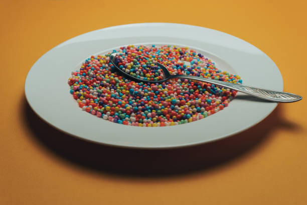 istock White plate and spoon with color preparations (vitamins, dyes, flavor enhancers, nutritional supplements, innovative technologies, candy sweets) on an orange background. 1143494212
