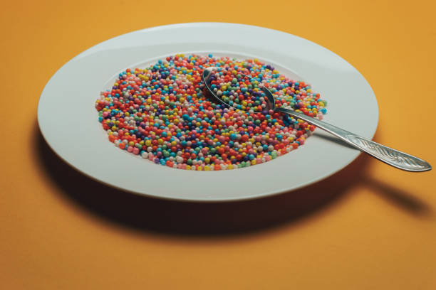 istock White plate and spoon with color preparations (vitamins, dyes, flavor enhancers, nutritional supplements, innovative technologies, candy sweets) on an orange background. 1143494302