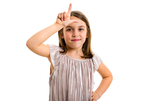 Portrait of happy girl making loser hand gesture at camera. Portrait of a cheerful cute little child girl looking at the camera, smiling showing L sign offensive gesture. Isolated on white background