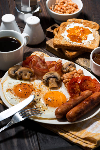 istock Fried eggs with bacon, sausages and vegetables, vertical 1143501143