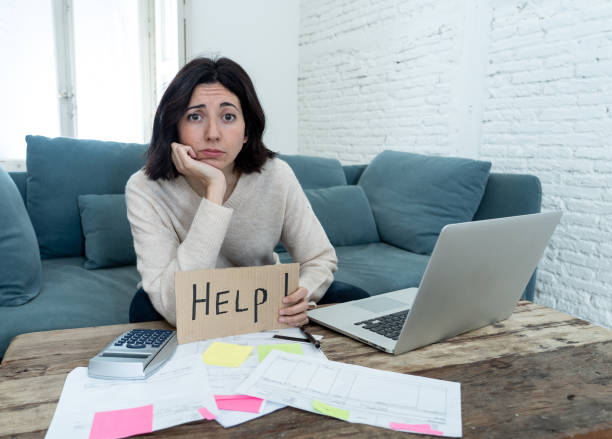 Portrait of worried young woman feeling stressed and desperate asking for help in paying bills, debts, tax expenses and accounting home finances with laptop. In online banking and financial problems. stock photo