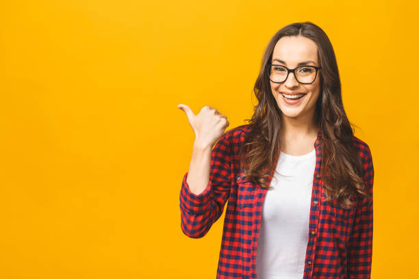 istock Image of happy young lady standing isolated over yellow background. Looking camera pointing. Thumbs up. 1143509679