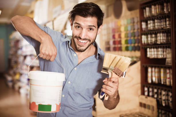 Man standing amongst racks in paint store with brushes and paint