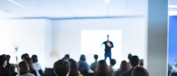 Photo of Business Conference Photo. Executive Speaker on Stage. Business Presentation Presenter Speech at Tech Entrepreneur Meeting. Corporate Event Audience. Expert Seminar Lecture Conference Event. Blurred.